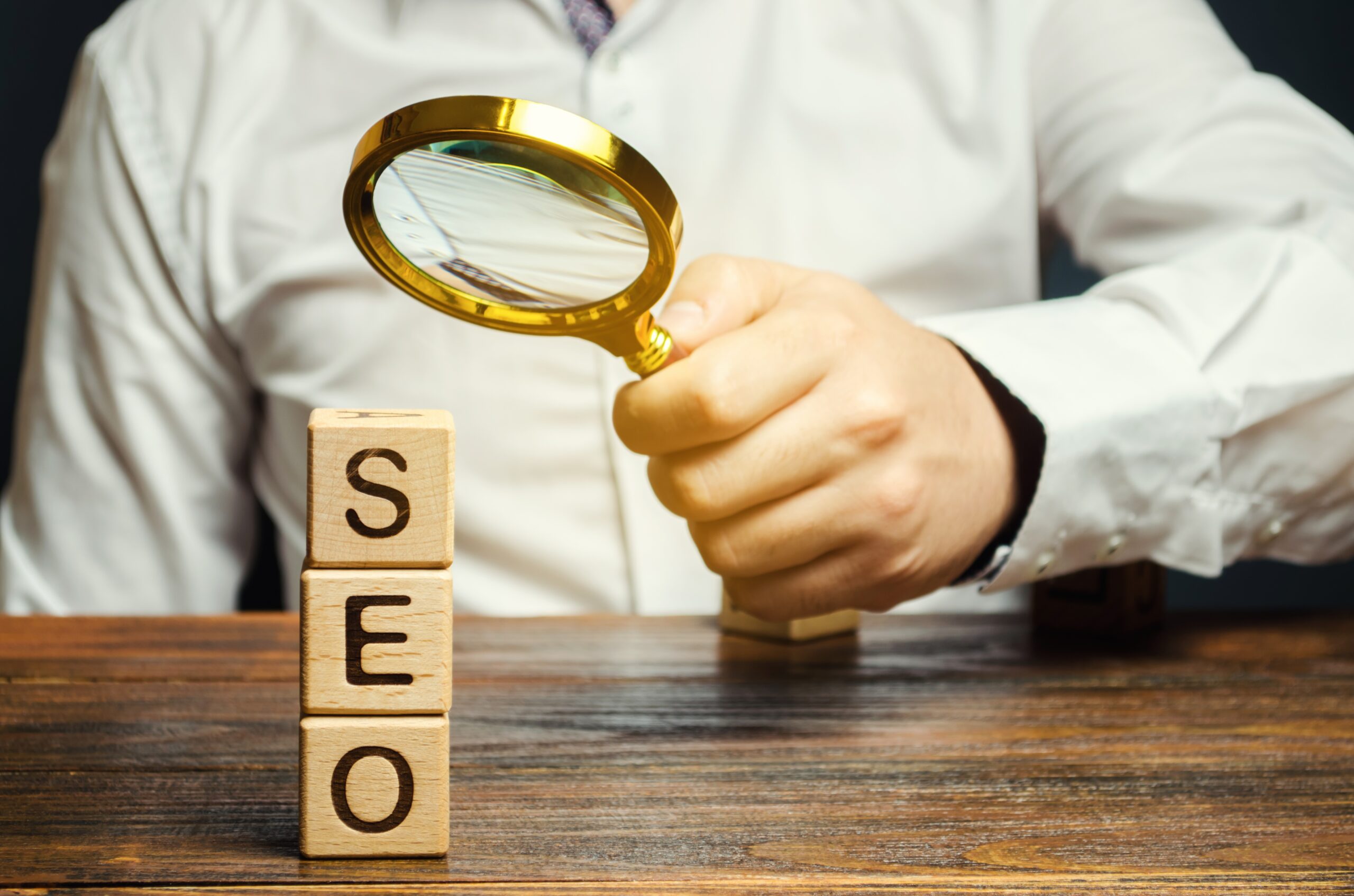Man holding a magnifying glass on a stack of blocks that spells out SEO